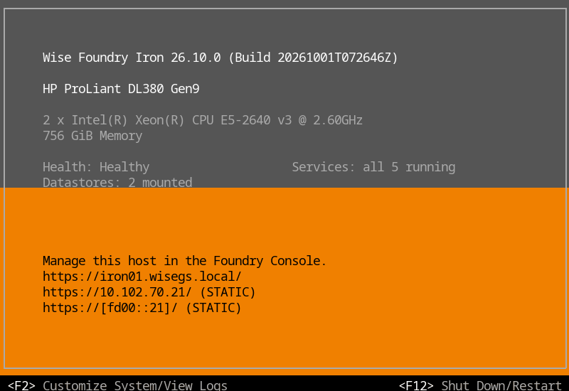Iron Console main screen of a Wise Foundry Iron 26.10.0 host in the boot screen's layout: its release, hardware, health, running services and mounted datastores on dark grey, and the addresses to manage it at, IPv4 and IPv6, on orange, with F2 and F12 in the footer